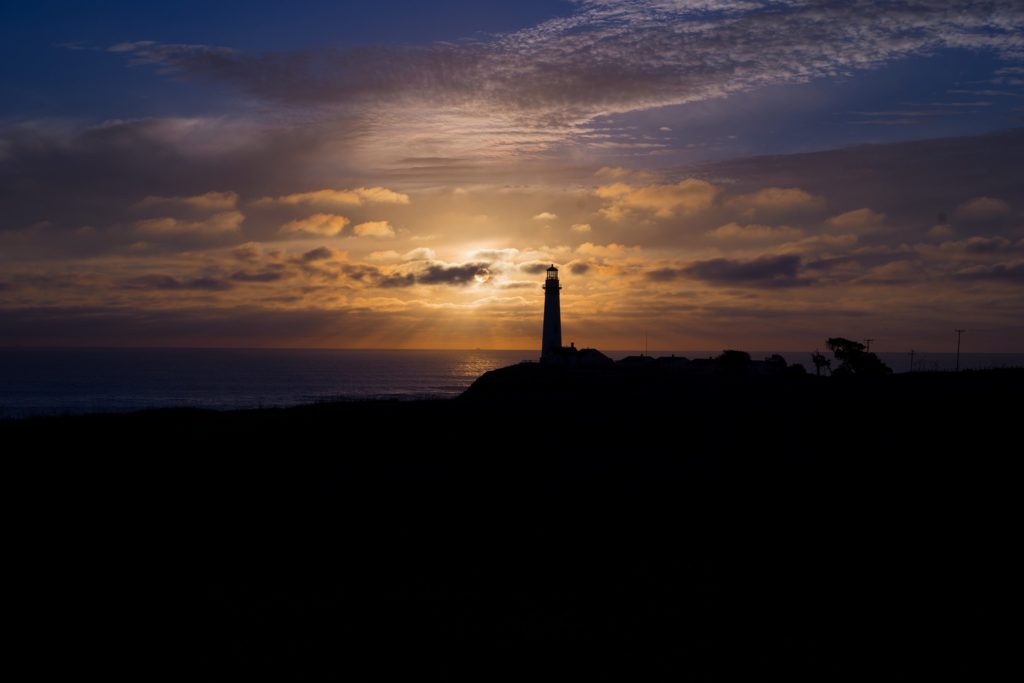 writing through grief: a lighthouse is silhouetted against a sunset; the sky and surroundings are dark