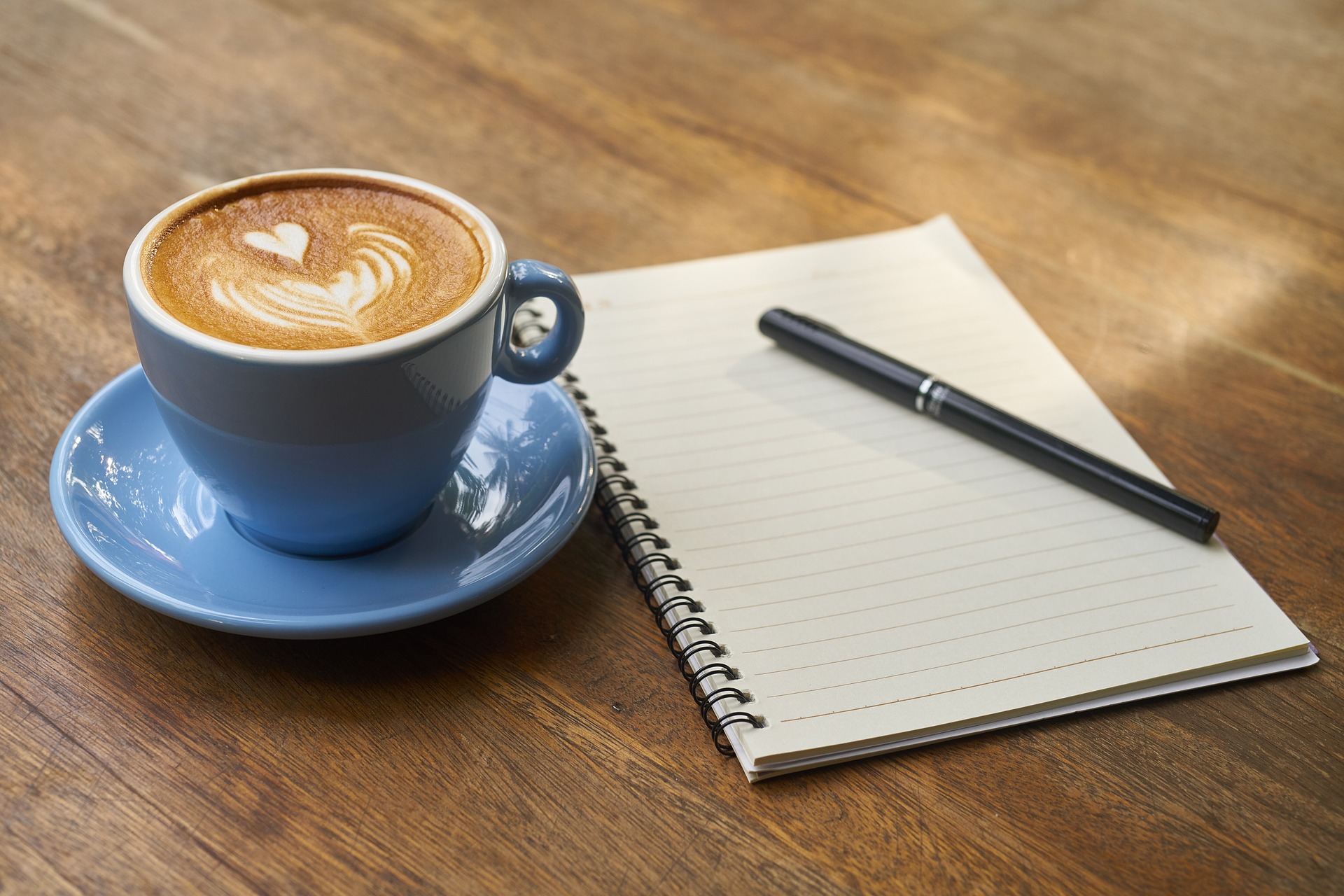 reasons to write: coffee, a blank notebook, and a black pen lie on a wooden table waiting to be enjoyed