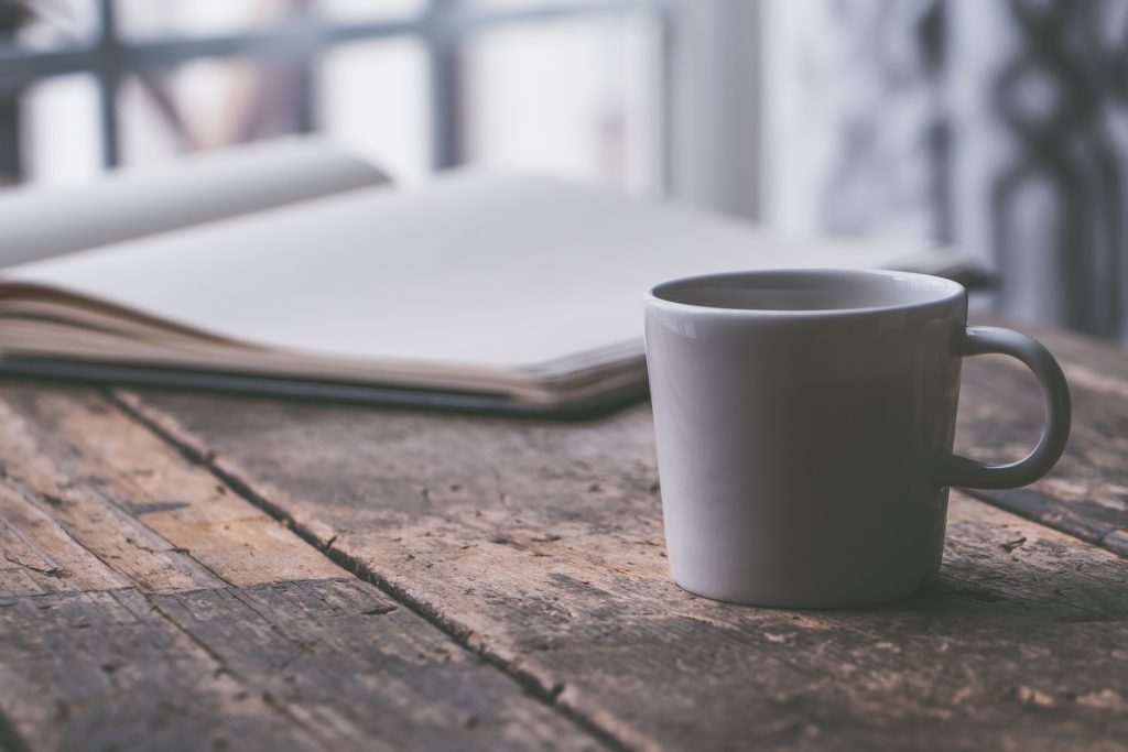 keeping a journal: an open journal and a white coffee mug rest on a rough, wood table