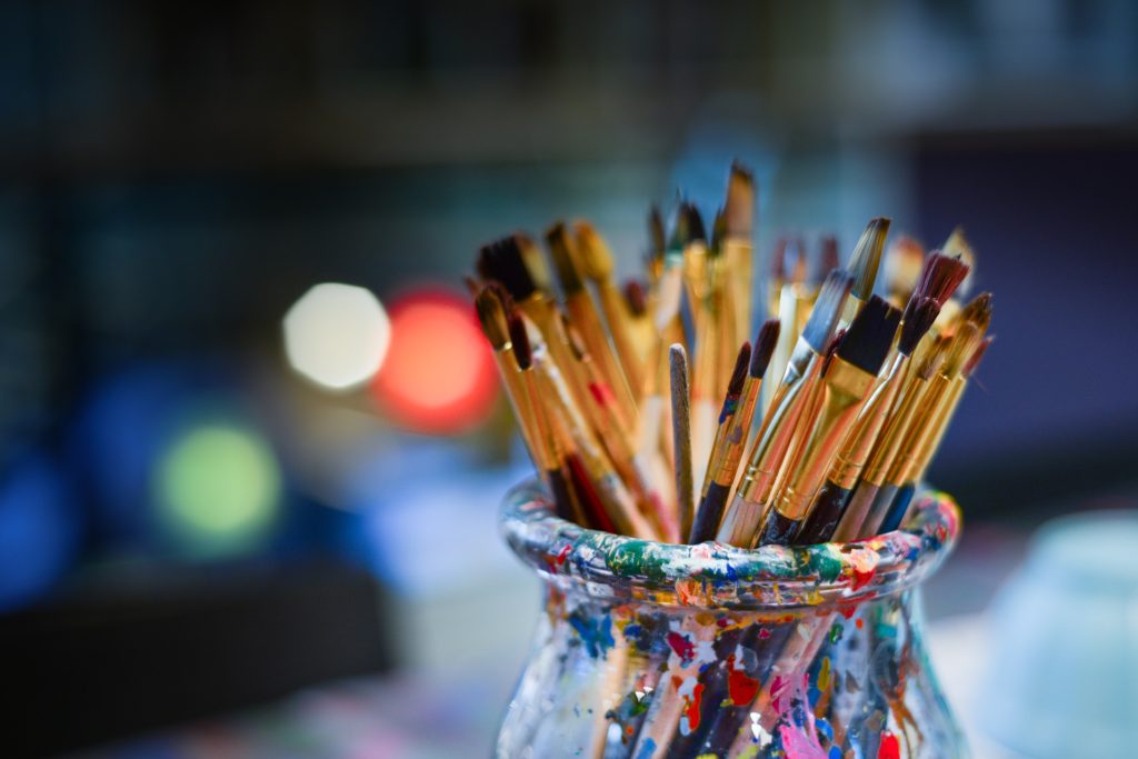 develop your creativity: paint-splattered jar with paintbrushes, soft background