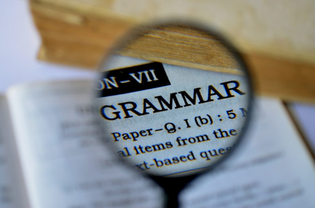 grammar police: magnifying glass examining papers that say GRAMMAR