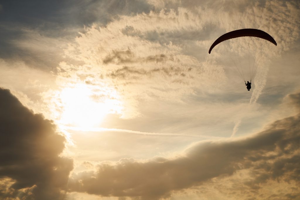 try something new: a parachutist floats through a golden, sun-and-cloud-filled sky